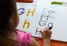 A photo of a young elementary student practicing writing their letters using a dry-erase marker.